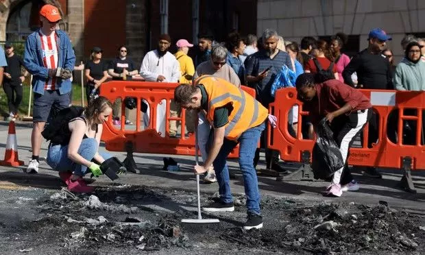Personas limpiando la acera después de los disturbios.
