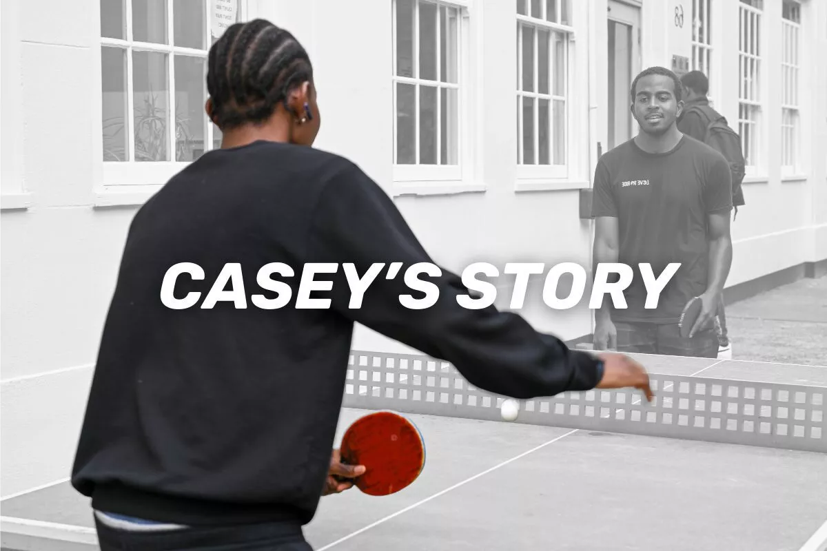 Imagen de un joven negro jugando al tenis de mesa, de espaldas a nosotros.