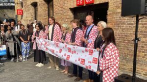 Photo of 7 people holding a banner with Uniqlo logos on it, with scissors to cut the banner to open the new store. Each person is wearing a red and white kimono