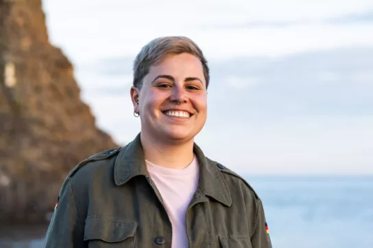 Young adult gender neutral with short hair - joyful smile against a seaside backdrop - serene outdoor moment captured at dusk.